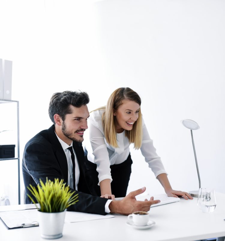 Business, startup and people concept - happy Caucasian creative team with PC computer in white office working together. Focusing on work. Handsome young man and brown hair female looking on monitor and typing something while sitting on working place in creative office.